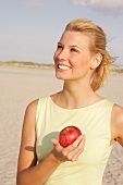 Jennifer Frau am Strand steht seitlich mit e. Apfel in der Hand