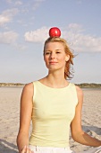 Jennifer Frau meditiert am Strand mit einem  Apfel auf dem Kopf