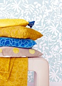 Close-up of pile of cushion on leather stool against blue floral wallpaper
