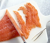 Salmon fillet being sliced with knife on cutting board