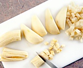 Peeled pears and bananas being chopped in cubes with knife on cutting board