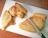 Chicken being chopped in pieces with knife on cutting board