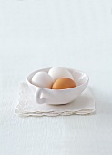 Close-up of two white eggs and one brown egg in cup