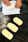 Pieces of butter being wrapped in butter paper on wooden table