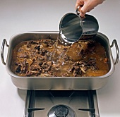 Water being poured to mixture in roasting pan, step 6