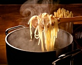 Spaghetti werden mit einer Holzlöf- fel aus dem Kochtopf entnommen