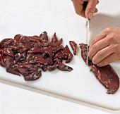 Close-up of hands cutting boar liver into thin strips on cutting board, step 1