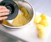 Slicing thin slices of potatoes with vegetable slicer in bowl