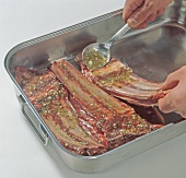 Close-up of hands applying mixture on spare ribs in baking dish, step 3