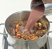 Adding broth to meat in pot while preparing wild boar ragout, step 5
