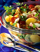 Close-up of potato salad with broad beans, tomatoes, cucumbers and sausage in glass bowl