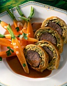 Close-up of venison fillet in puff pastry with carrots on plate