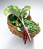 Basket with rhubarb, pea pods and spinach on white background