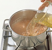 Adding juice to dark sauce in pot for preparation of beuschel, step 2