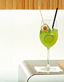 ein grüner Cocktail mit Gurken- scheiben und Cocktailkirsche