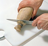 Close-up of hands cutting ends of lotus root on chopping board, step 1