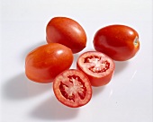 Whole and halved red oval plum tomatoes on white background