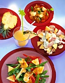 Various pineapple dishes on red plates and glass of pineapple juice
