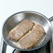 Meat slices being fried in pan, step 1
