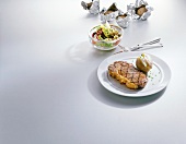 Beef rump steak with baked potato on plate and salad in bowl