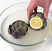 Close-up of artichokes with lemon slice in glass bowl with ice and water, step 7