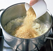 Adding cup of rice to onions and oil in pot
