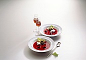 Beef with jellied consomme on two plates and glasses of wine on white background