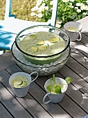 Bowl and cups with zucchini gazpacho in bowl with ice cubes on wooden surface