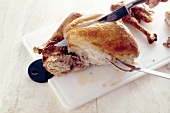 Baked chicken being cut with knife and carving fork on chopping board, step 3