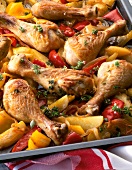 Close-up of cooked chicken legs with potatoes, pepper and other vegetable in baking tray