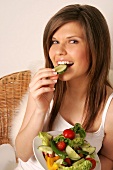 Portrait of woman with long hair eating cucumber slice, smiling