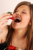 Portrait of woman with long hair eating strawberry, smiling, close-up