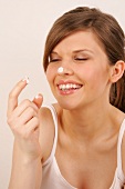 Pretty woman with brown hair applying cream on her nose with finger, smiling