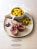 Lamb chops with saffron and raisin rice in cup with wooden fork on plate