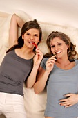 Two women lying on bed and biting green hot chilli pepper and red hot chilli pepper