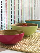 Three bowls in pink, green and blue colour on wicker mat