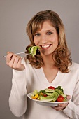 Portrait of beautiful woman eating lettuce with fork while holding salad dish, smiling