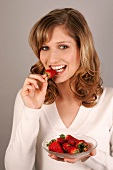 Portrait of young woman biting strawberry while holding plate of strawberries, smiling