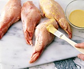Mustard sauce being applied on pieces of rabbit's legs with brush