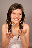 Close-up of pretty woman with brown hair cleaning her face with water, smiling