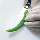 Green chilli being slit lengthwise with knife, step 5