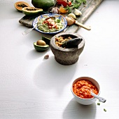 Bowls of hot sauces, guacamole, chilli sauce with papaya on white background