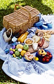 Picnic basket, fruits, cheese, sausage and bread on blue blanket