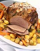 Close-up of leg of lamb with carrots, garlic and rosemary on plate