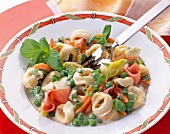 Tortellini with cream sauce, hams and peas on plate