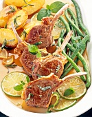 Close-up of lamb chops with green beans, rosemary potatoes and limes on serving dish