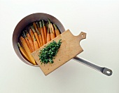 Cooked carrots with herbs in frying pan against white background