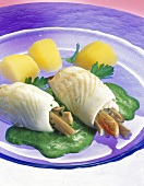 Two plaice rolls with spinach sauce and potatoes on glass plate