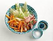 Sliced vegetables in bowl with salt and peppers on white background
