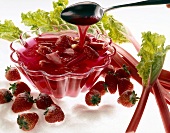 Red jelly with strawberries and rhubarb in transparent bowl on white background